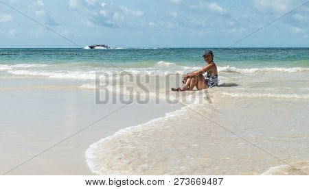 Woman Sitting In Water At Beach In Hat And One Piece Bathing Suit