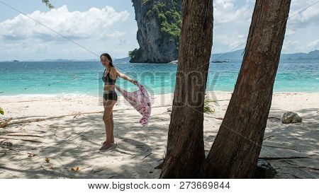 Young Woman Standing On Tropical Beach Holding Towel And Islandn In Background