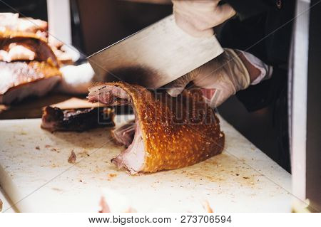 Close Up View Of Hands Chopping Roast Pig Ribs With A Large Meat Cleaver