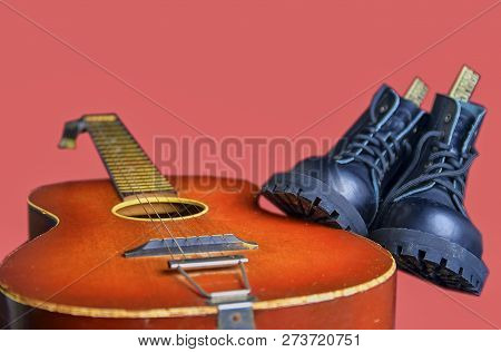 Rock And Roll Concept. Black Boots And Acoustic Guitar. Rock And Roll Boots On Pink Background.