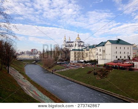 View Of The Church And The Buildings Behind The River, Covered With Ice, Against The Blue Sky With C