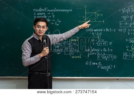 Asian Teacher Giving Lesson Over The The Physics Formular In Thai Laguage On Black Board In School C
