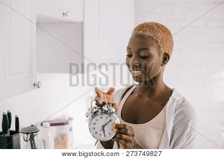 Beautiful African American Woman With Short Hair Holding Clock In White Citchen