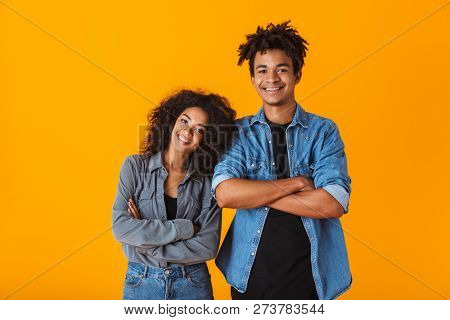 Happy young african couple wearing casual clothes standing isolated over yellow background, arms folded