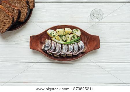 Marinated Herring, Potatoes And Onions In Earthenware Plate With Glass Of Vodka And Rye Bread On Whi