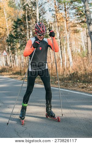 Training An Athlete On The Roller Skaters. Biathlon Ride On The Roller Skis With Ski Poles, In The H
