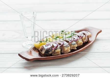 Marinated Herring, Potatoes And Onions In Earthenware Plate With Glass Of Vodka On White Wooden Back