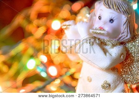 Figurine Of Little Angel With Golden Shiny Wings And Halo That Plays Flute On Shining Background Of 