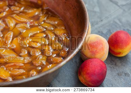 Fresh Bright Peaches And Nectarins Lay On The Kitchen Desk Close To The Copper Jar, Full Of Peach Ja