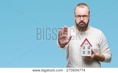 Young caucasian real state agent man holding house isolated background with open hand doing stop sign with serious and confident expression, defense gesture