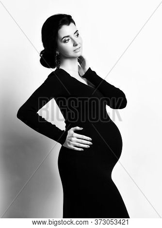 Black And White Portrait Of Beautiful Pregnant Woman Standing Side To Us In Black Elegant Dress Hold