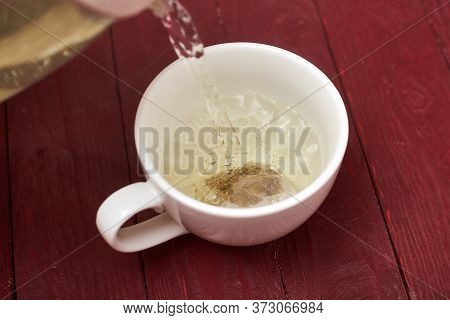 Tea Bag In A White Cup. Add Boiling Water To The Cup. Making Delicious Herbal Tea.