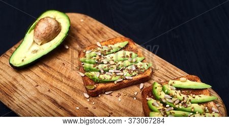 Toast With Sliced Avocado, Mixture Of Seeds On A Wooden Background. Healthy Snack Tomorrow. The Conc