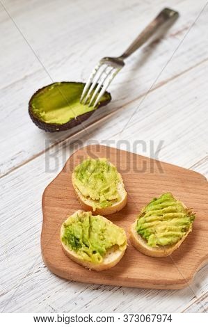 Baguette, Bruschetta, Canapes With Avocado On A Light Wooden Background.