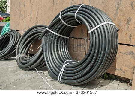 A Rolled Up Black Industrial Rubber Hose Tied With Rope On The Street. Products For Irrigation Syste