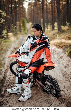 Beautiful Young Female Racer Sitting On Her Motocross Bike On A Trail Of Sand In The Woods