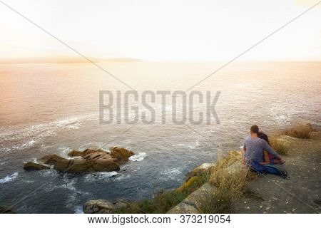 Couple In Love Watching The Sunset On A Cliff With The Sea Of Background