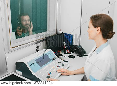 Audiologist Woman Doing The Hearing Exam To A Mixed-race Man Patient Using An Audiometer In A Specia