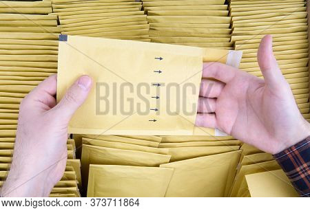 Male Hands Open A Yellow Bubble Envelope Against The Open Shipping Box Full Of Padded Mailers. Close