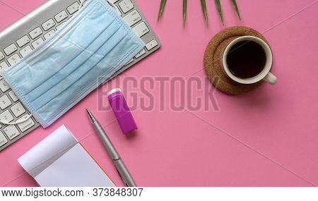 Top View Of Pink Office Desk With Keyboard, Medical Face Mask, Coffee And Stationery. Copy Space.