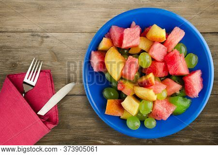 Fruit Salad On A Brown Wooden Background. Vegetarian Salad Of Fruit On A Blue Plate With Fork Ank Kn