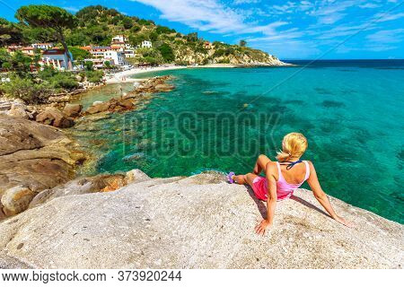 Woman In Pink Swim Suit Resting And Sunbathing Over The Stone Along Sant Andrea Beach, Elba Island. 