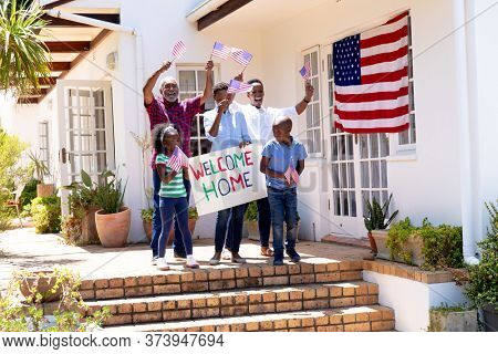African American three generation family standing by their house with a banner, welcoming a solider coming back home.