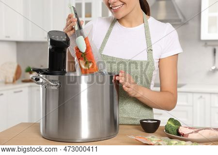 Woman Putting Vacuum Packed Salmon Into Pot With Sous Vide Cooker In Kitchen, Closeup. Thermal Immer