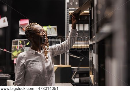 African American Woman Detective Taking Csi Report File From Rack With Folders. Law Enforcement Inve