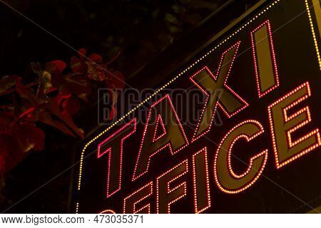 Neon Red Electric Inscription Taxi Office On The Facade Of The Building.
