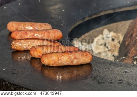 Pork Sausages Ready To Eat, Grilled Or Roasted In A Barbecue On An Open Fire And Flames, In A Street