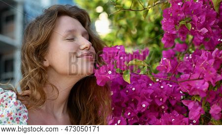 Portrait Of Happy Beautiful Girl, Young Positive Woman Is Smelling Beautiful Pink Flowers In The Gar
