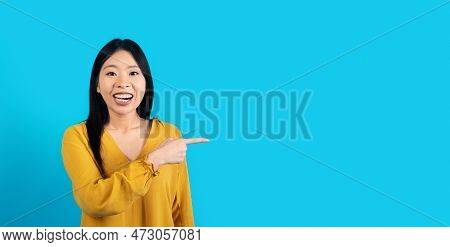 Excited Young Asiam Lady Pointing At Copy Space On Blue