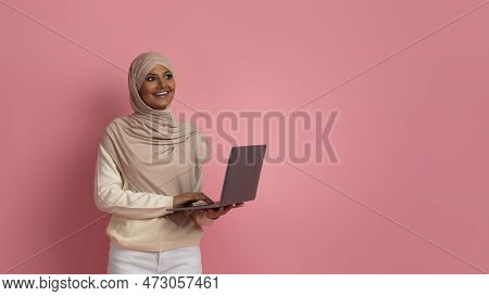 Pensive Young Muslim Woman With Laptop In Hands Standing Over Pink Background