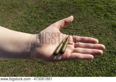 Two Rifle Cartridges In Hand Against The Background Of Green Grass. Close-up