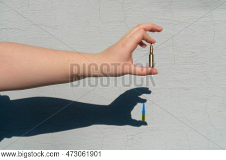 Rifle Cartridge In Hand. Hand Shadow Forms On Wall. Shadow From The Cartridge Has A Yellow-blue Colo