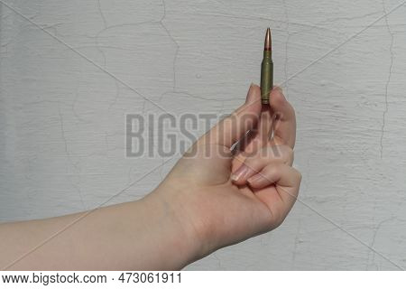 Rifle Cartridge In Hand Against The Background Of A White Concrete Wall. Close-up