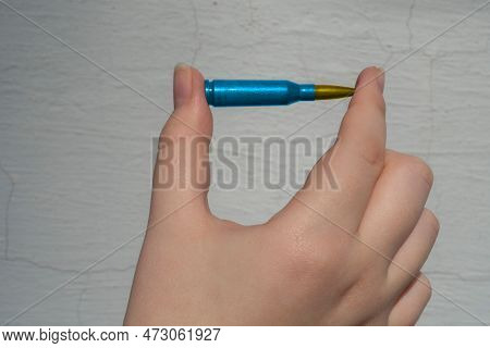 A Yellow-blue Rifle Cartridge In A Hand Against A White Wall (national Symbols Of Ukraine). The Conc