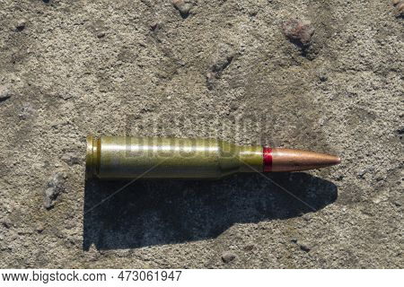 A Rifle Cartridge Lies On A Concrete Surface (close-up). Horizontal Orientation