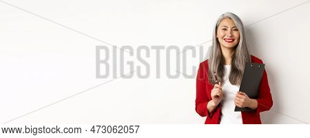 Successful Asian Lady Boss In Red Blazer, Holding Clipboard With Documens And Pen, Working And Looki