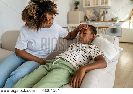 Worried Caring African American Mom Touch Forehead Of Sad Child Sitting On Couch Feeling Unwell Mala