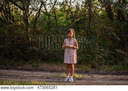 Teenage Girl With Green Hair Got Lost In Forest. Child Stands Frightened On The Path In Ray Of Light
