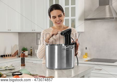 Woman Using Thermal Immersion Circulator At Table In Kitchen. Sous Vide Cooking