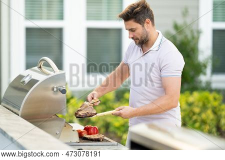 Man Cooking Meat On Barbecue In The Backyard Of The House. Handsome Man Preparing Barbecue. Barbecue
