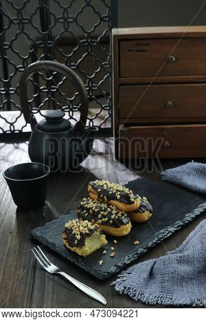 Delicious Chocolate Choux Cake On Black Plate With Coffee Cup On Wooden Table