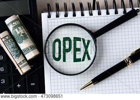 Letters Opex (operating Expense) Under A Magnifying Glass On A White Notebook Against The Background