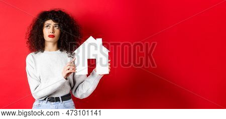 Real Estate. Sad Woman Thinking Of Buying Own House, Showing Paper Home Cutout And Looking Up With U