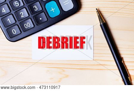 On A Light Wooden Background, A Black Calculator, A Pen And A Business Card With The Text Debrief