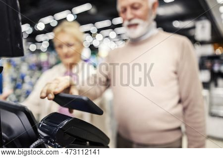 Close Up Of Senior Man Using Mobile App For Checkout On Self Service Register In Supermarket.