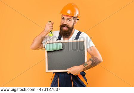 Smiling Man Housepainter In Helmet And Work Clothes Hold Paint Roller And Blackboard